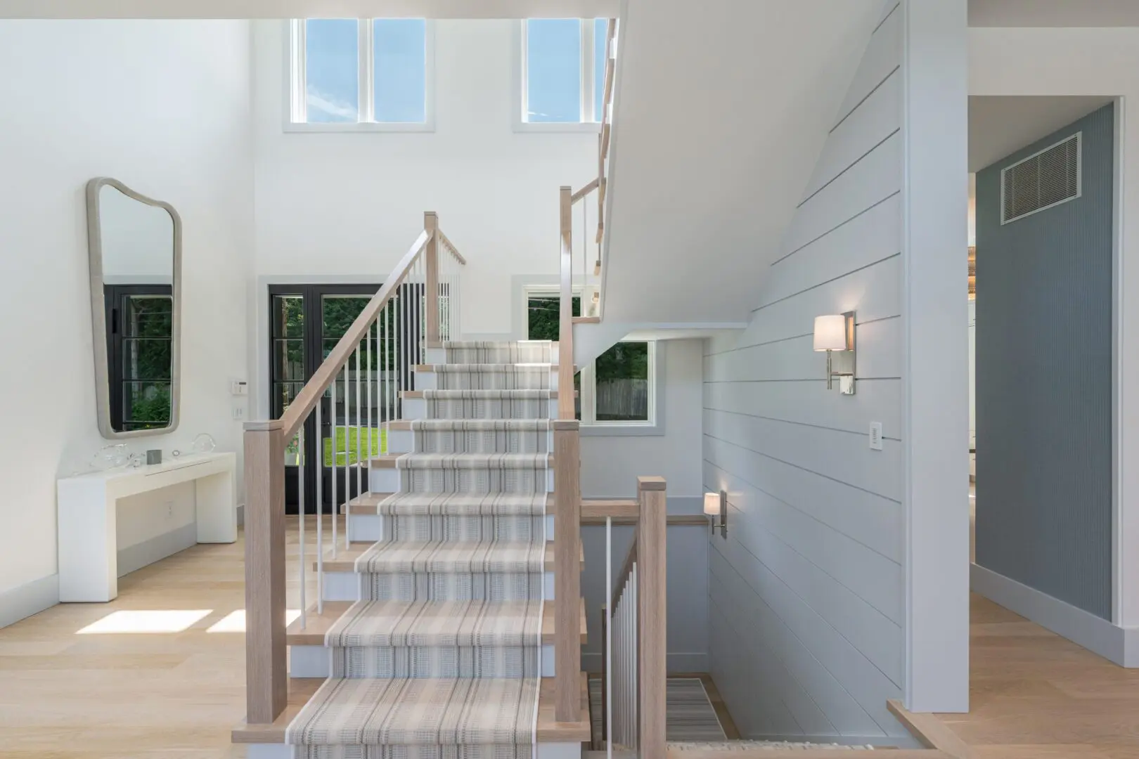 Bright staircase with plaid carpet runner and natural wood railing in a modern home.