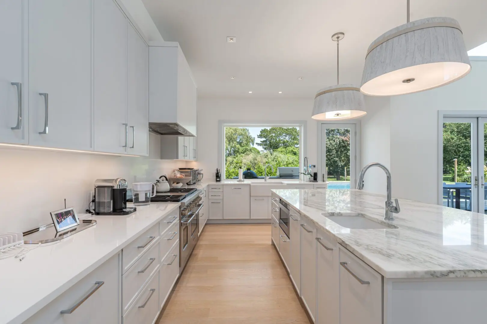Bright modern kitchen with white cabinetry and large windows.