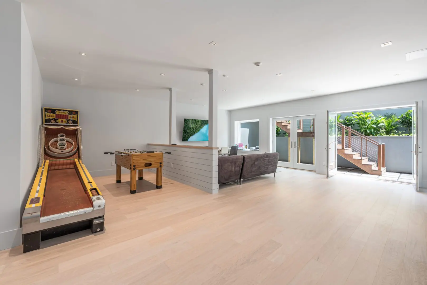 Spacious modern game and lounge room with large windows and light wood flooring.