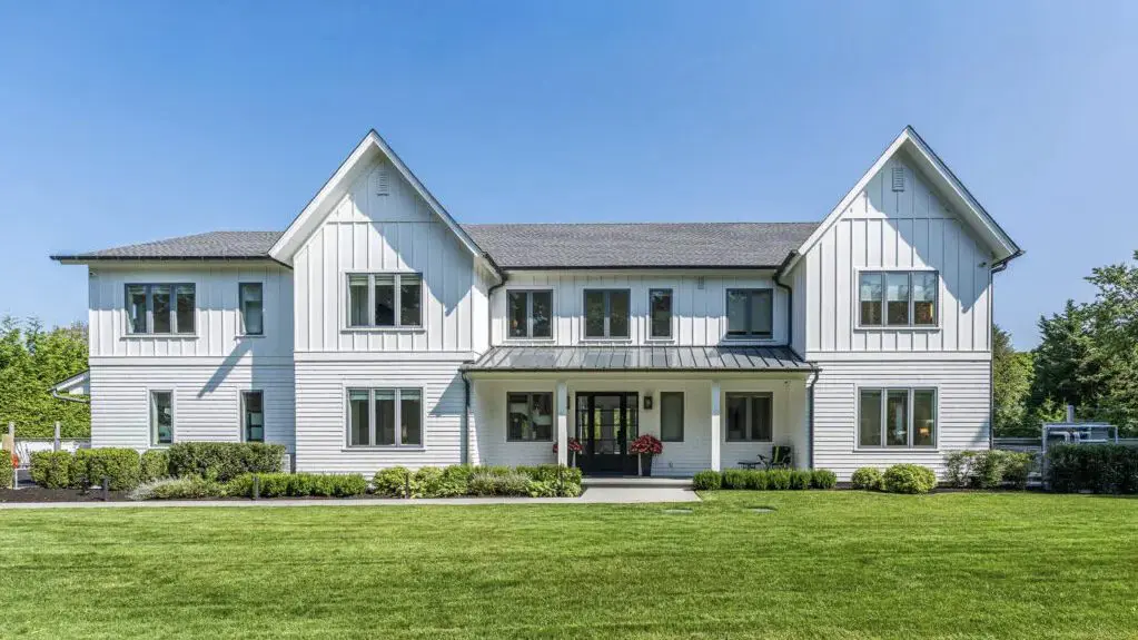 Modern white farmhouse with large windows and a manicured lawn.