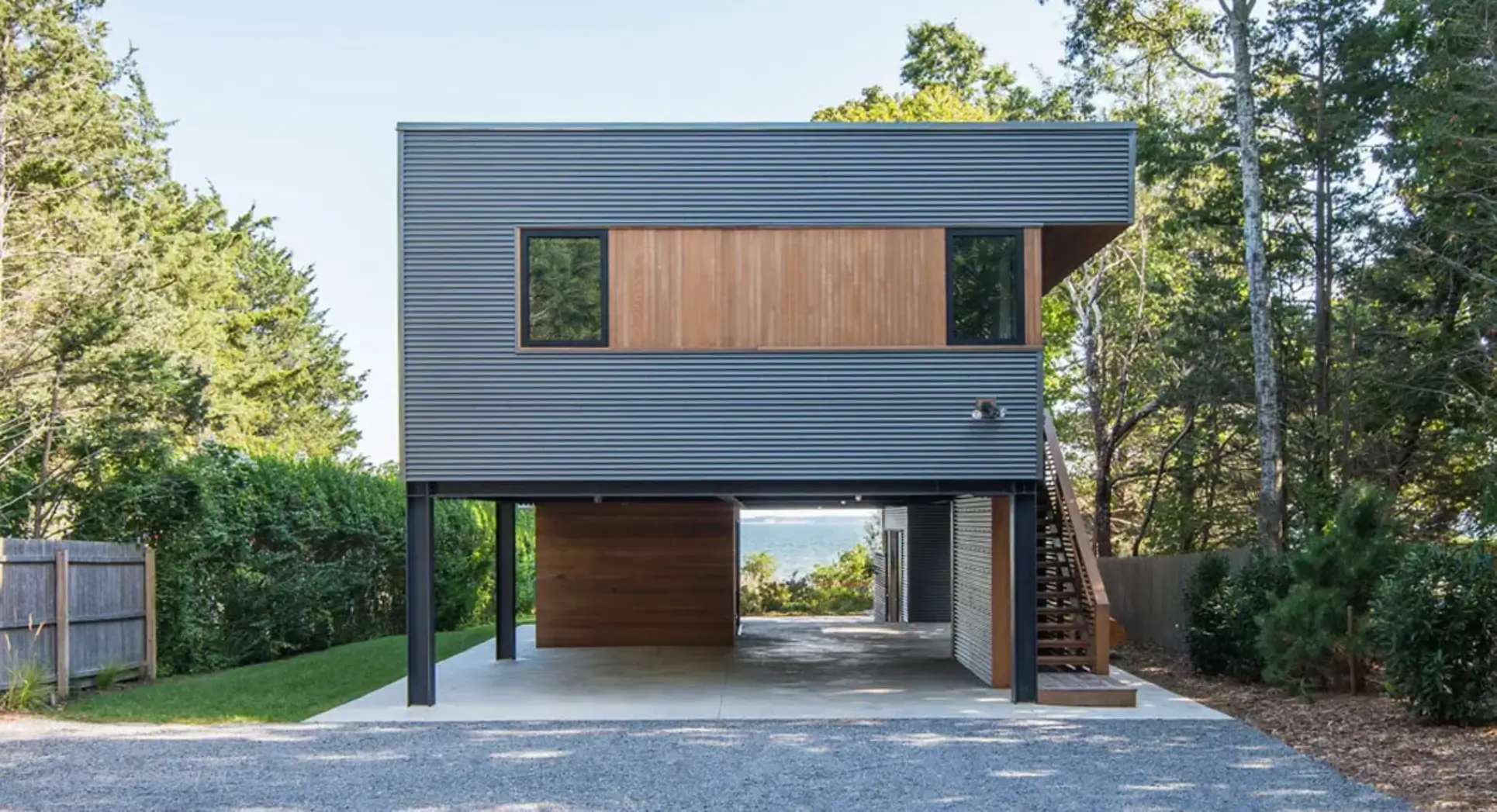 Modern house with black exterior and wooden accents, featuring large windows and an elevated structure.