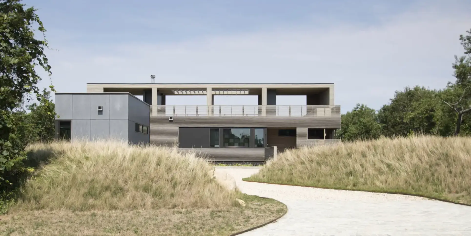 Modern house with large windows and a pathway through grassy dunes.