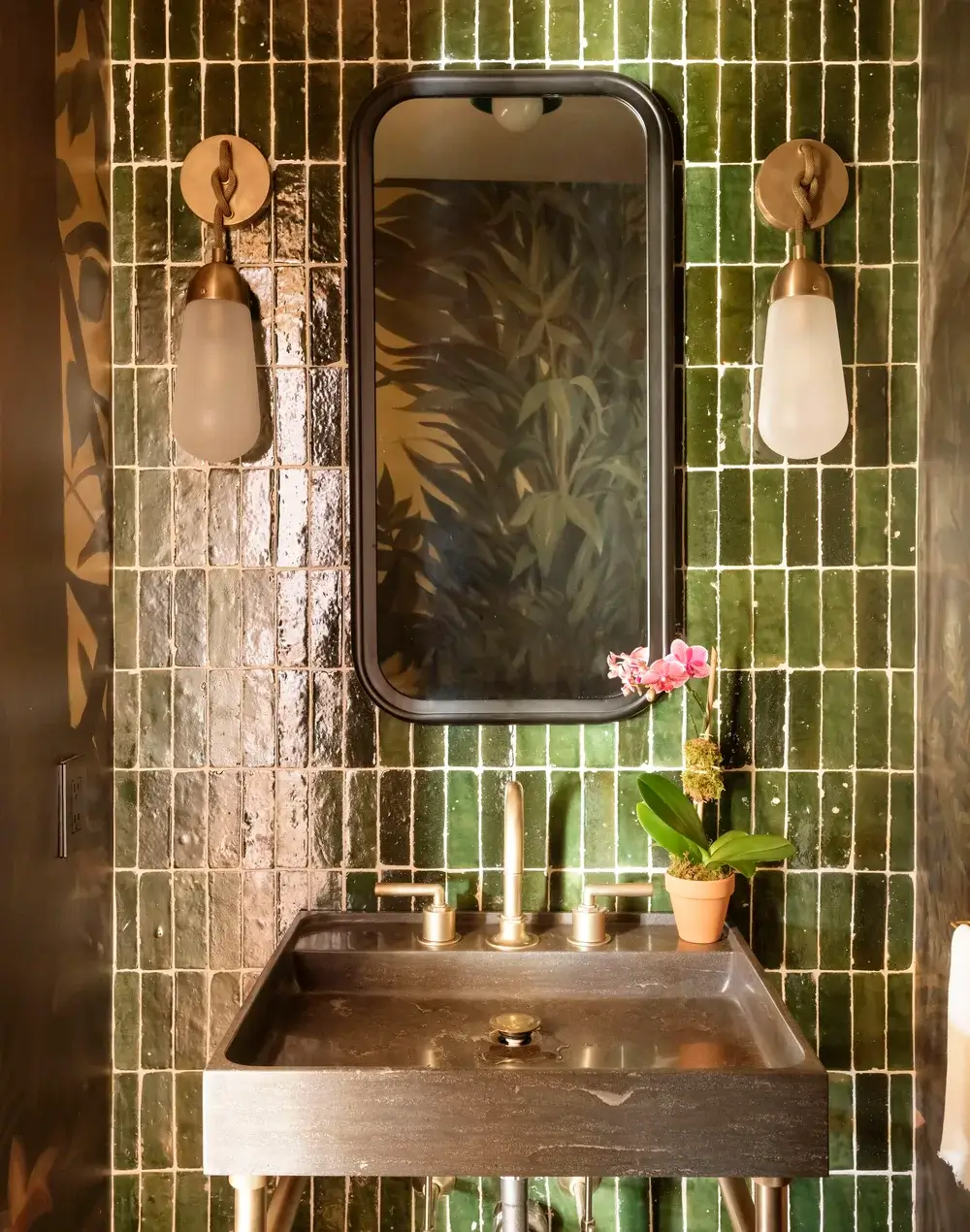 Elegant bathroom sink area with green tiles and pink orchid.