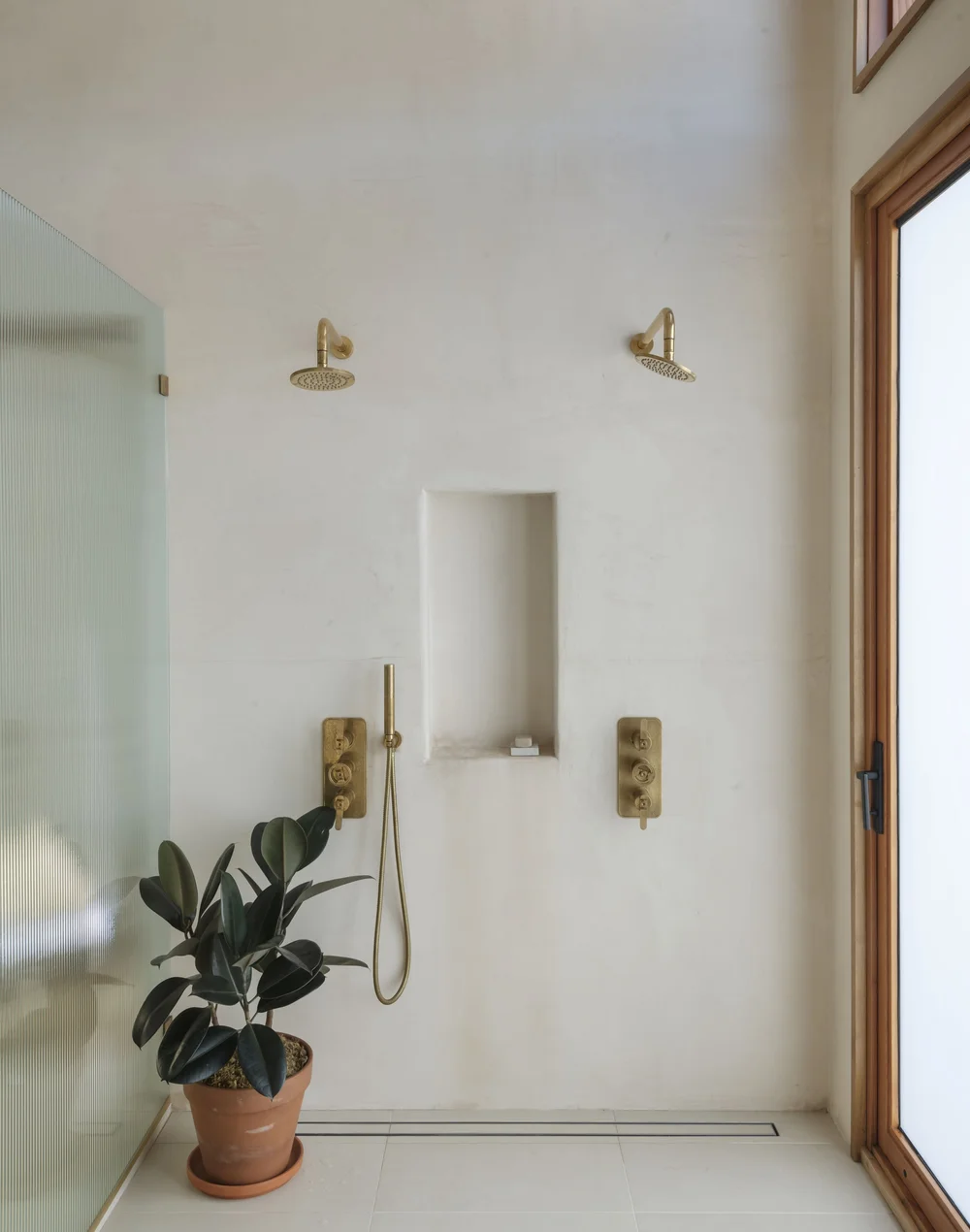 Minimalist bathroom shower area with plant and wooden accents.